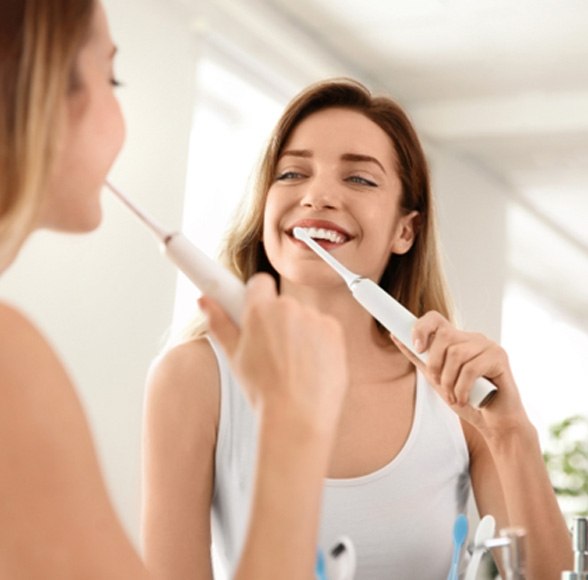 Woman smiling and brushing her teeth in bathroom mirror