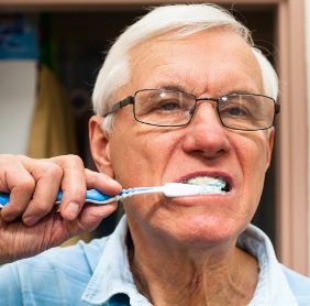 Man with dental implant tooth replacement brushing teeth