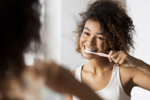 Woman smiling as she brushes her teeth in the mirror